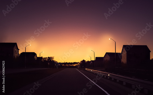 Silhouettes of houses by a road during pinkish sunset