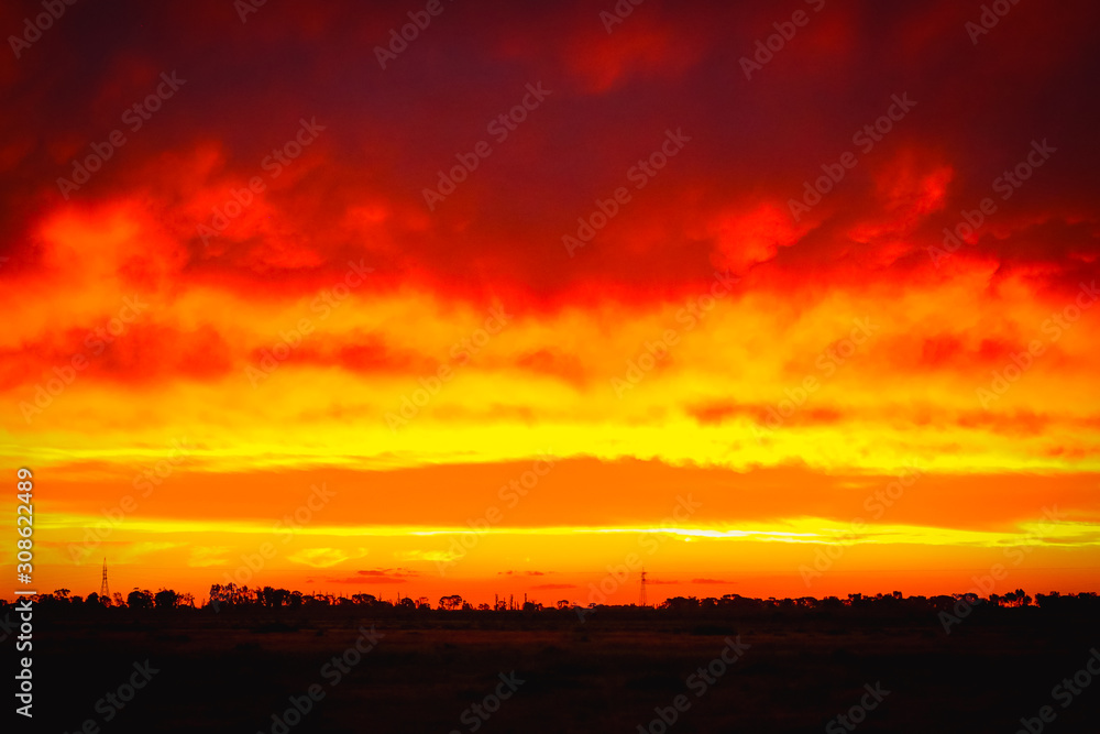 Fiery sunset sky in Central Victoria with power line structured towering along the horizon