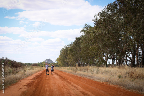 Two young brothers mucking around on dirt country road with view of Pyramid Hill in the distance. Central Victoria, Australia.