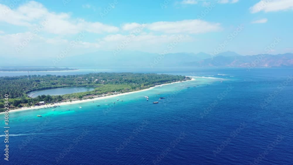 Peaceful sea scenery of blue azure lagoon around shore of tropical island with boats anchored near white beach on bright sky with white clouds in Bali Peaceful sea scenery of blue azure lagoon around shore of tropical island with boats anchored near white beach on bright sky with white clouds in Bali