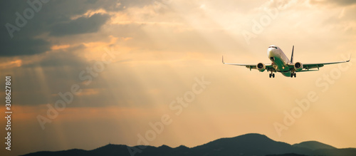 Passenger airplane. Landscape with Front of white airplane is flying in the orange sky with clouds over mountains, sea at colorful sunset. Passenger aircraft is landing. Commercial plane. Private jet