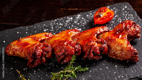 Mexican food concept. Baked chicken wings with spicy tomato salsa on a black board, on a wooden table. background image. copy space