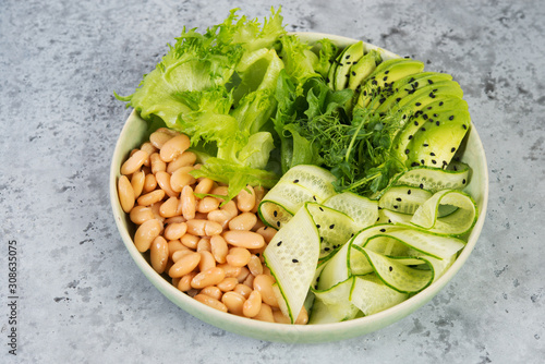 Vegetarian green salad bowl with fresh vegetables and canned white beans on a gray concrete background. Horizontal photo