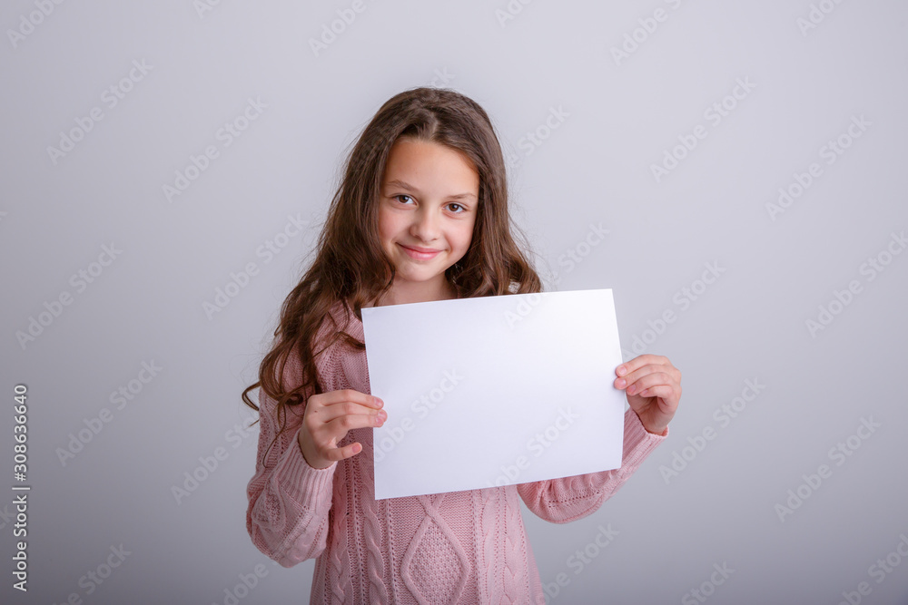 beautiful little brunette girl holding a white sheet of paper on a white background, smiling, surprised beautiful little brunette girl holding a white sheet of paper on a white background, smiling, surprised