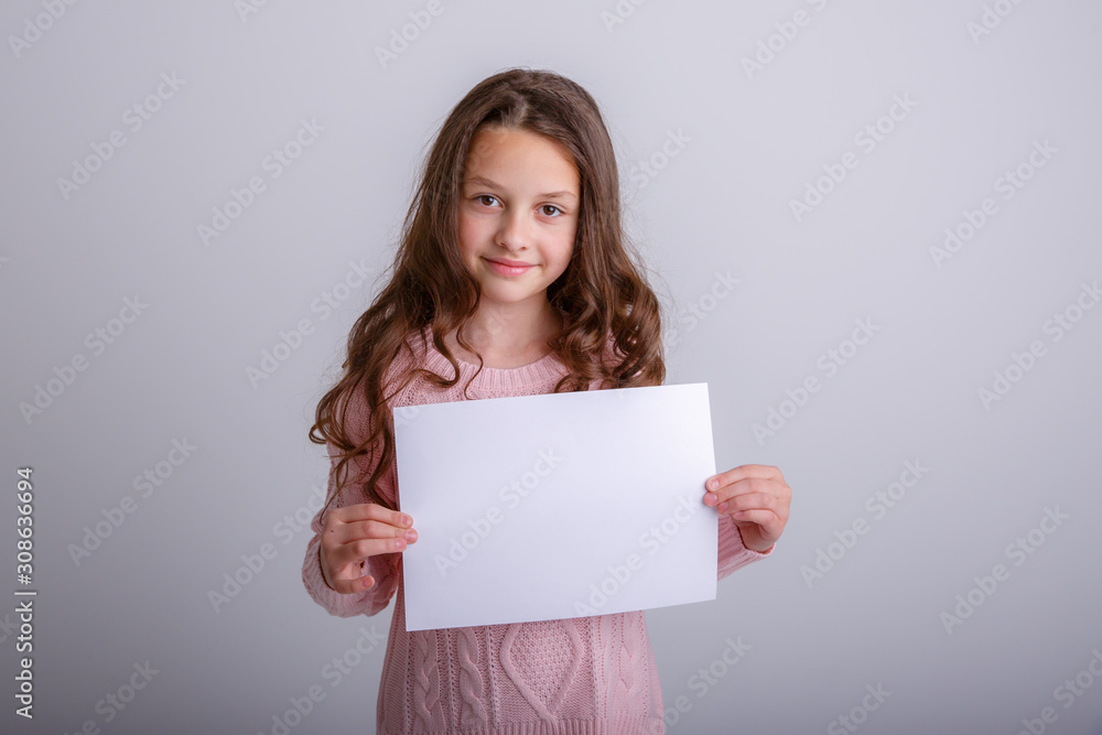 beautiful little brunette girl with a white sheet of paper on a white background, smiling, surprised beautiful little brunette girl with a white sheet of paper on a white background, smiling, surprised