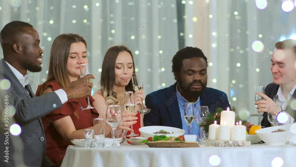 Multi-ethnic company colleagues sit at a table at a corporate holiday. They talk, drink champagne and celebrate the new year. Blurred garland Multi-ethnic company colleagues sit at a table at a corporate holiday. They talk, drink champagne and celebrate the new year. Blurred garland