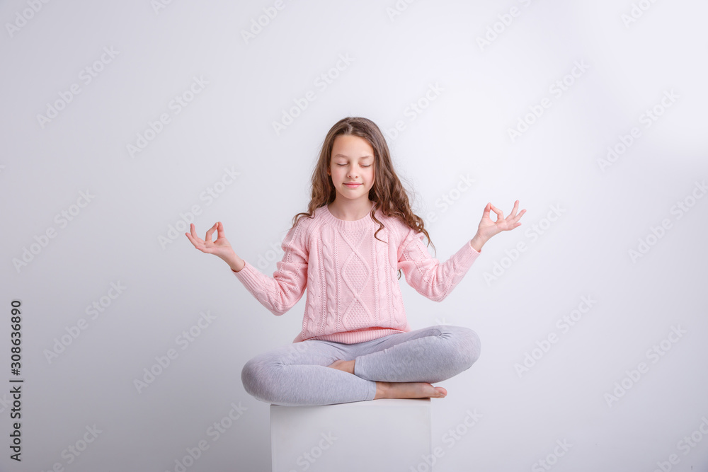 a little brunette girl sits on a cube in a meditative pose isolated on a white background a little brunette girl sits on a cube in a meditative pose isolated on a white background
