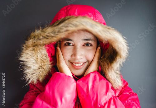 Portrait of a freezing woman in winter cloth standing isolated on a gray background.Smiling girl touching her face wearing winter coat warm clothes.