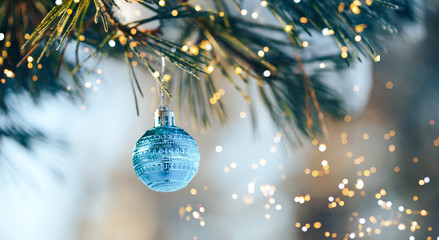 blue christmas ball hanging on branch on sruce tree outdoor, snow, winter, with decorations.