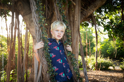 Portrait of young boy wearing Christmas shirt playing on swing made of fig tree roots covered in mistletoe  photo