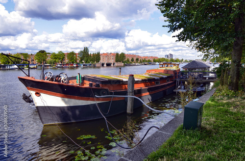 Amsterdam, Holland, August 2019. View of the Amstel River, outskirts of the city. A large moored boat is used as a houseboat. Sunny day with blue sky and white clouds.
