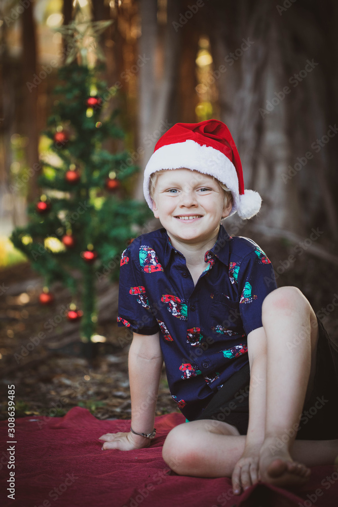 Child dressed in Christmas outfit on red blanket in the park with a decorated Christmas tree in the background Child dressed in Christmas outfit on red blanket in the park with a decorated Christmas tree in the background