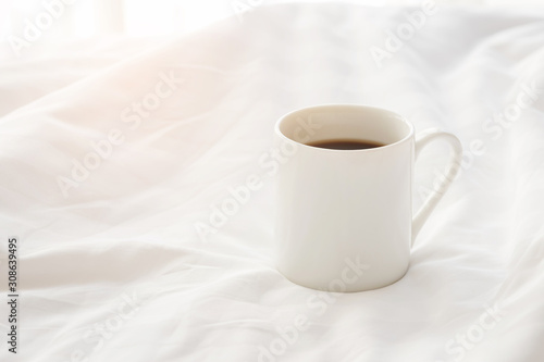 Black coffee cup on the unmade bed in cozy morning with sunshine into window.