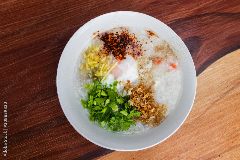 Rice congee with soft-boiled egg flavor with pickled chili vinegar and ground dried chilies on wooden table. Rice congee with soft-boiled egg flavor with pickled chili vinegar and ground dried chilies on wooden table.