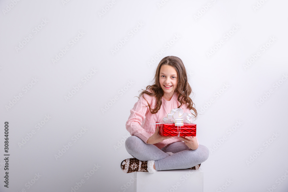 little girl is smiling with a gift in her hands sitting on a white cube isolated on a white background little girl is smiling with a gift in her hands sitting on a white cube isolated on a white background