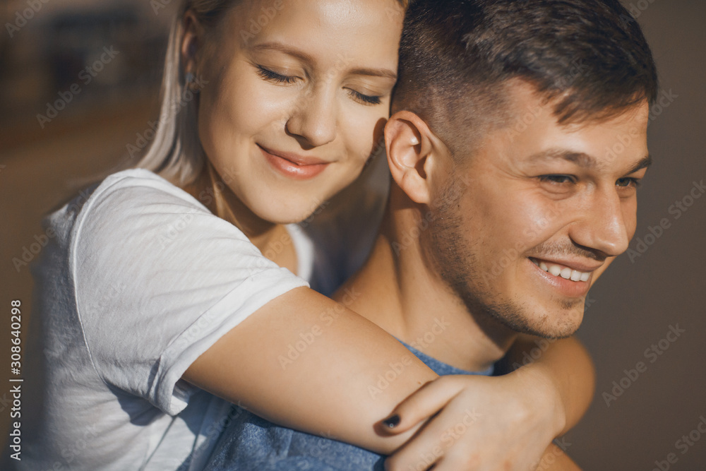 Close up portrait of a lovely blonde woman embracing from back neck of her man with closed eyes smiling in the kitchen.