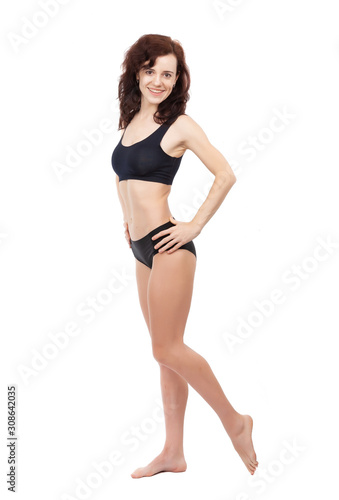A barefoot girl in a black sports swimsuit is standing on a white background.