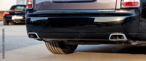 Close-up of a black luxury car bumper of an sedan with two side turbo exhaust pipes outdoors on asphalt. Auto service industry. Air and environment pollution. photo