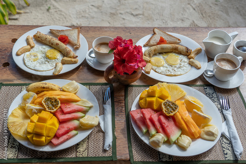 Tropical breakfast of fruit, coffee and scrambled eggs and banana pancake for two on the beach near sea