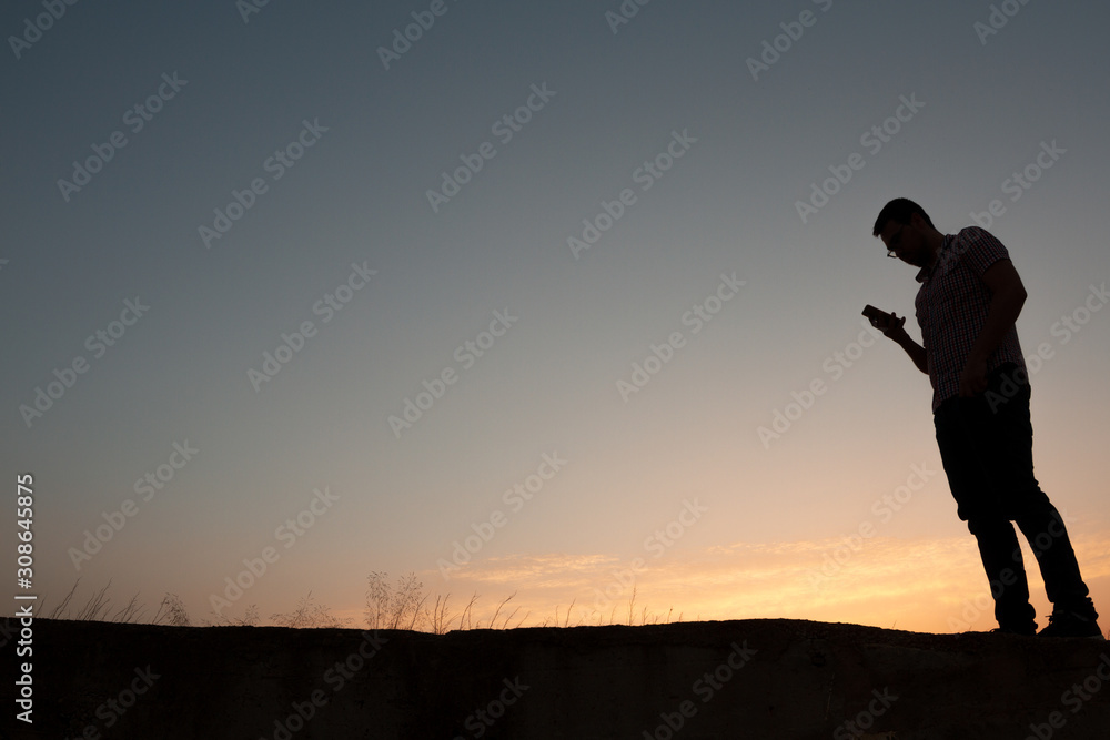 silhouette of man with cell phone at sunset