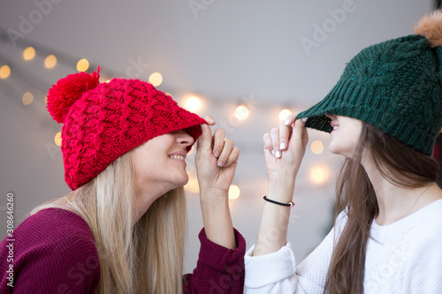 Two young woman wearing knitted hats in a room with the christmas lights decorations