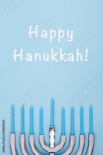 Blue background with menora and candles and Happy Hanukkah wording. Hanukkah and judaic holiday concept. Vertical