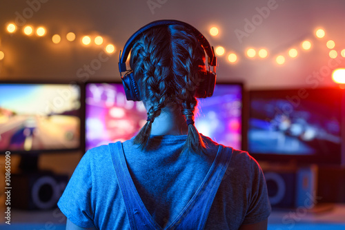 A girl plays video games at a computer. on the background of three monitors. Creative light