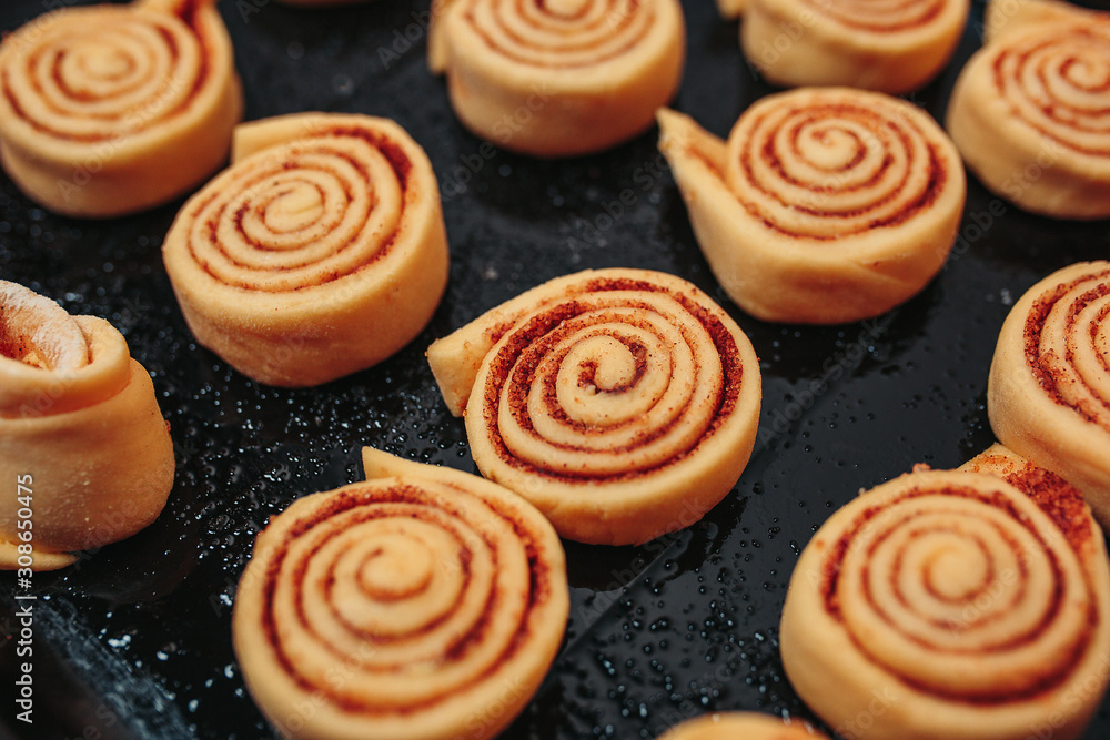Unbaked cinnamon rolls on the black baking pan on the orange background. Macro unbaked cinnamon rolls.