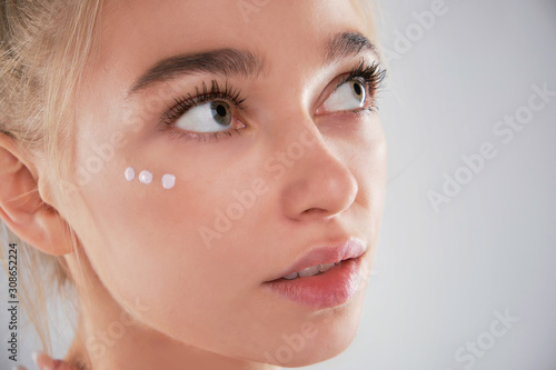 Portrait of woman with healthy face applying cosmetic cream under the eyes