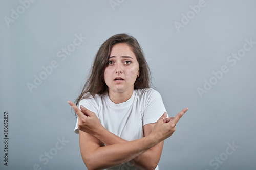 Obraz na plátně Girl in white t-shirt over isolated gray background undecided pointing fingers i