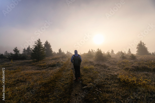 Man traveler standing with the sun in foggy on trail in forest