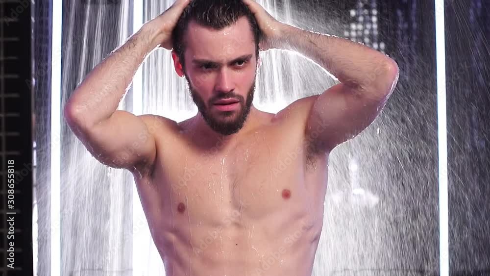 Young caucasian naked man take shower in Spa centre, raised hands on head standing under running water. Slow motion Young caucasian naked man take shower in Spa centre, raised hands on head standing under running water. Slow motion