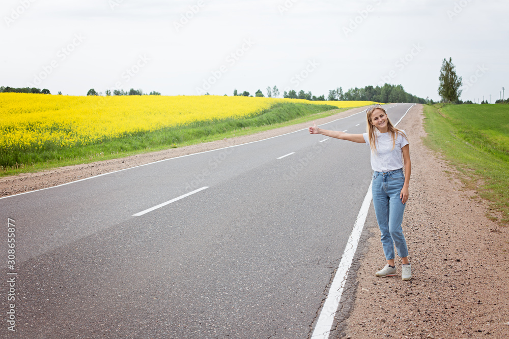 Fototapeta premium Girl with a smile votes on the road stopping the car