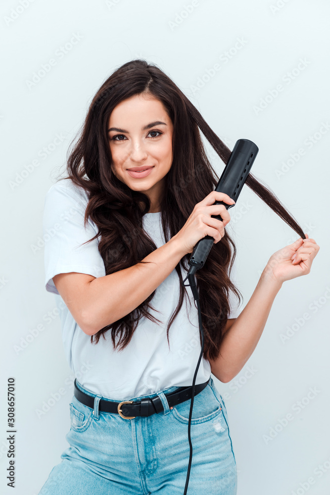 Smiling young woman straightening her hair with a straightener on the white background Smiling young woman straightening her hair with a straightener on the white background