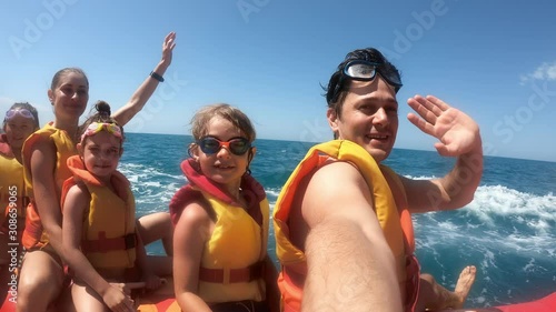 Happy people having fun in the sea on water attractions. Tourists on inflatable banana smiling and waving hands. Family on summer vacation
