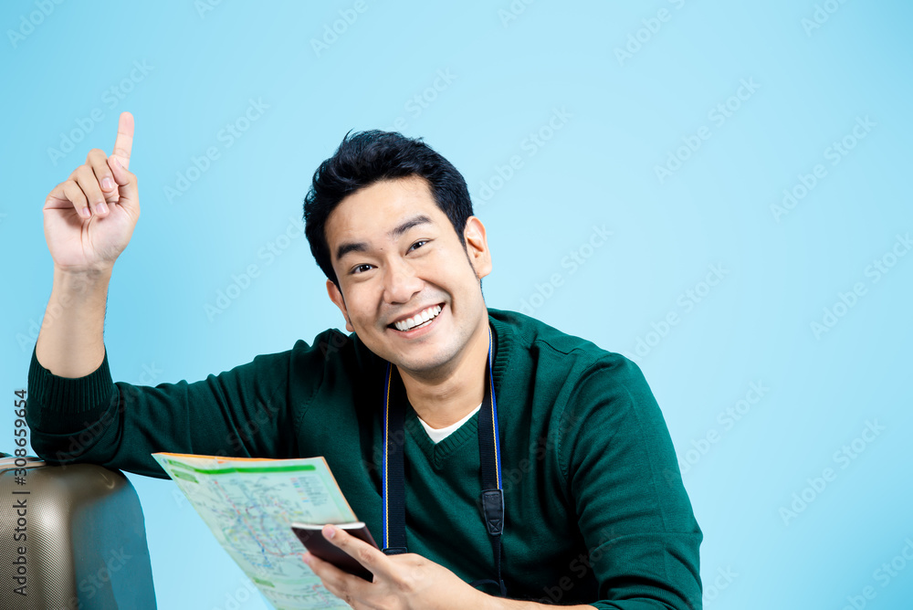 Happy Asian tourist sitting and reading map on blue background,