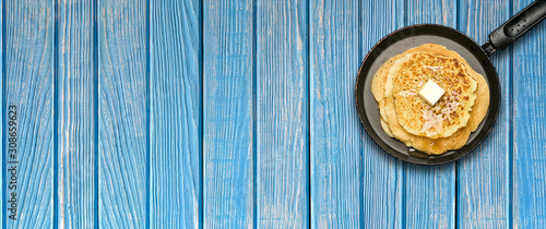 Hot delicious pancakes in frying pan on blue wooden table. Pancake week. Panoramic banner.