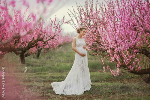 A woman in a long white wedding dress among the peach blossoming trees.