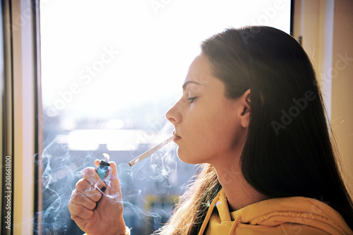  Beautiful attractive girl smoking a cigarette at the window. Pretty woman smoking cigarette.