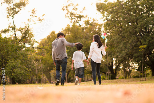 Scene from behind of Asian happy family spend time together walking and relaxing at the park in the afternoon autumn, concept family togetherness, warm hearted family, parenthood, happy family outing.