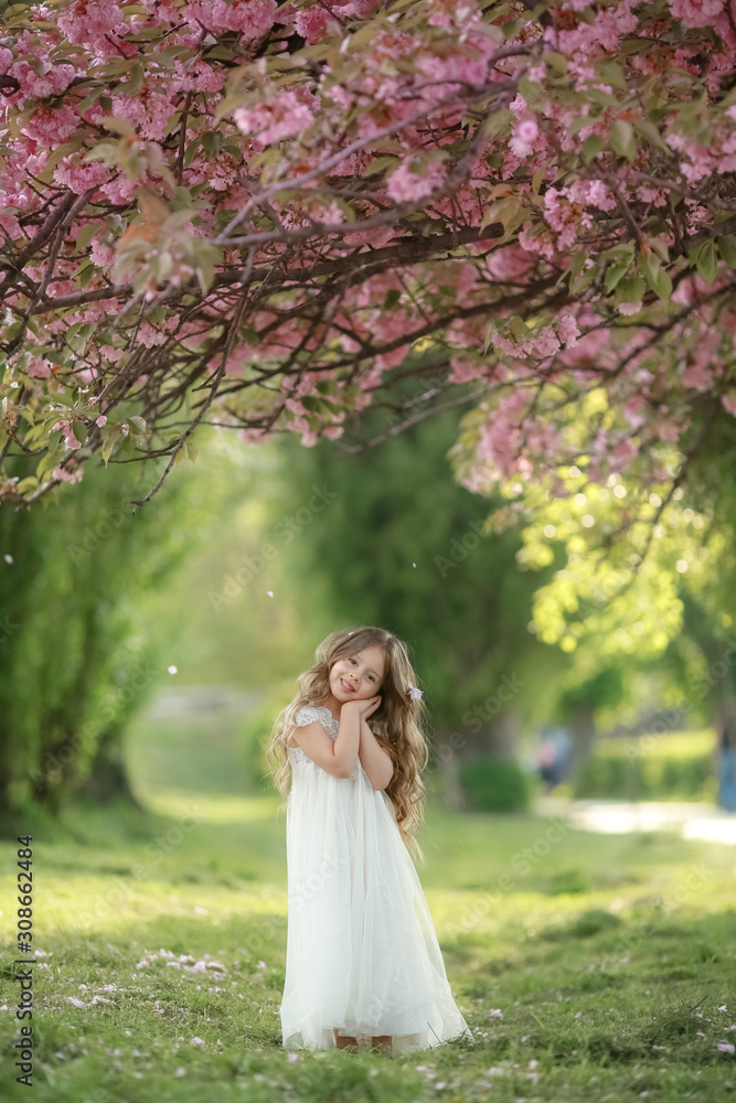 A child in a white preschool dress on the green grass in a public Park wearing a white dress. A child in a white preschool dress on the green grass in a public Park wearing a white dress.