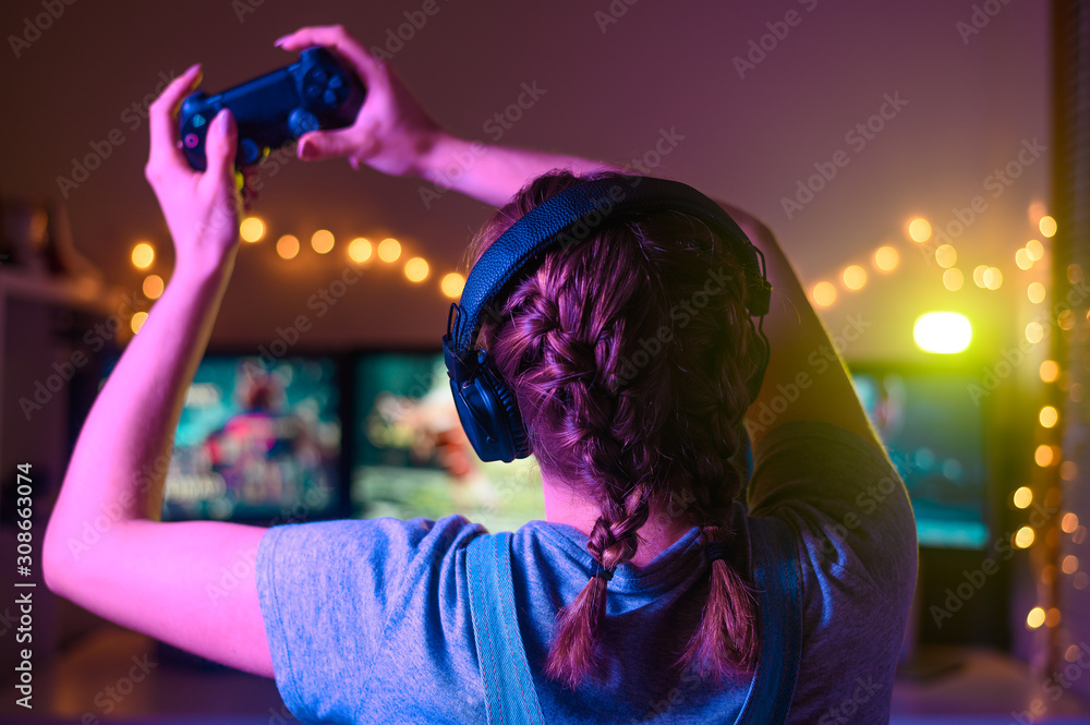 A gamer or a streamer girl at home in a dark room with a gamepad playing with friends on the networks in video games. A young man sits in front of a monitor A gamer or a streamer girl at home in a dark room with a gamepad playing with friends on the networks in video games. A young man sits in front of a monitor