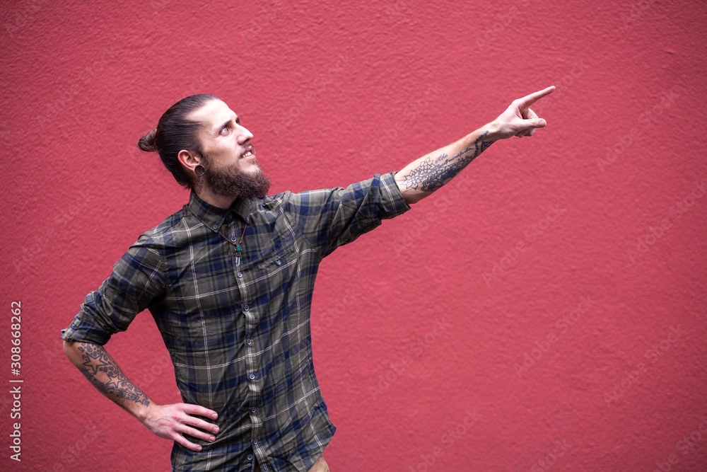 young man with beard and gauged pierced ears pointing in front of a red wall background