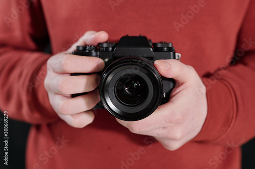 Hands of young male photographer in maroon sweatshirt holding new photocamera