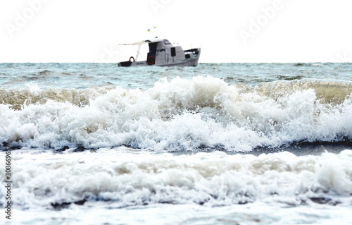 a white boat is visible from the shore in large sea waves
