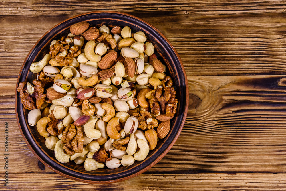 Various nuts (almond, cashew, hazelnut, pistachio, walnut) in ceramic plate on a wooden table. Vegetarian meal. Healthy eating concept. Top view Various nuts (almond, cashew, hazelnut, pistachio, walnut) in ceramic plate on a wooden table. Vegetarian meal. Healthy eating concept. Top view