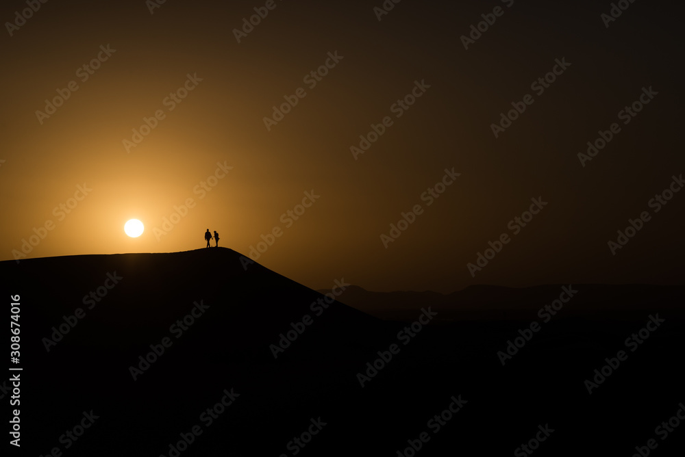 Fototapeta Silhouettes of two human people during sunset in the dunes of the Saharan desert.