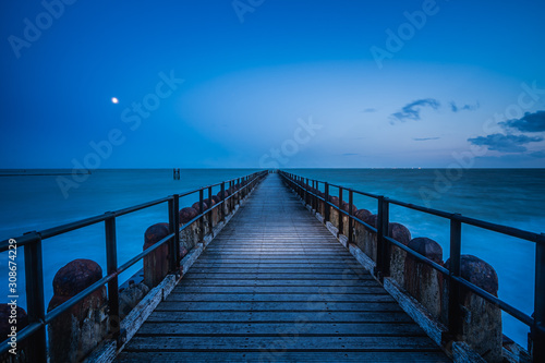Long wooden pier extends over water toward the horizon. A leading line to the horizone © fotografiecor
