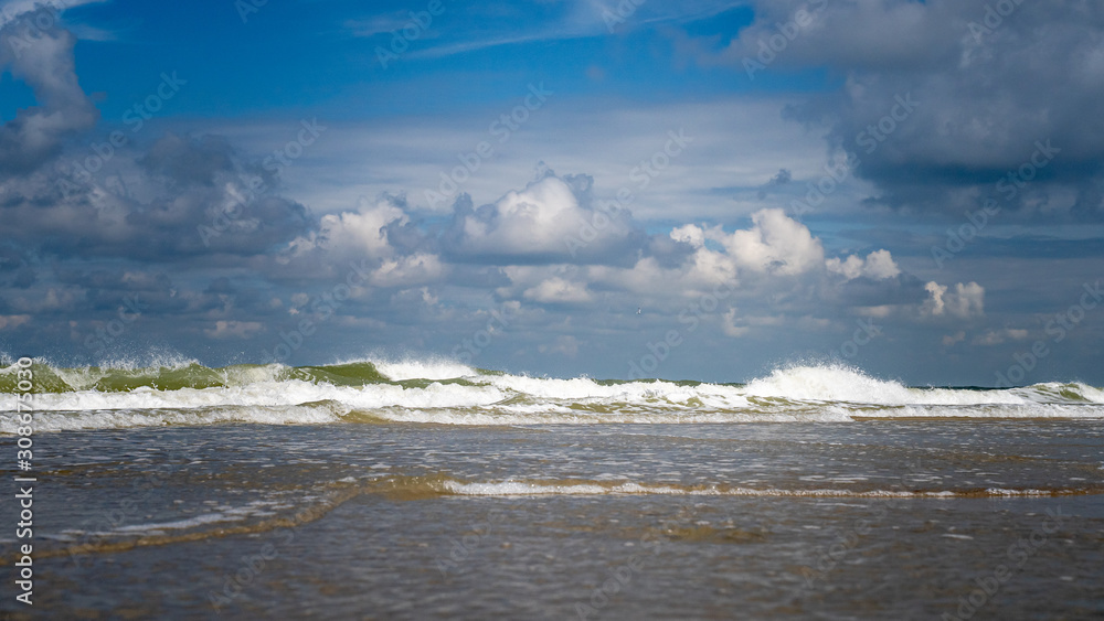 Splashing waves on the coast of the Netherlands with white foam heads on a calm summer day