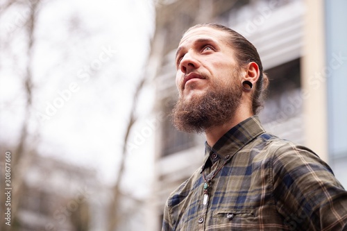 young man with beard and gauged pierced ears with buildings in background